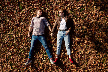 Cheerful young beautiful couple lying on the ground and holding hands in autumn park.