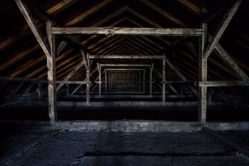 Fototapeta na wymiar Picture of an old dark and abandoned attic of a residential building with a focus on the decaying framework made of crumbling wooden beams and plywood