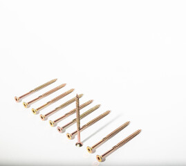 Construction metal screws of gold color on a white background lie in a row, and one stands. Self-tapping screws as a background. Place for text