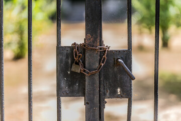 Metal gate at the entrance to a garden of a farm, broken lock closed with a rusty metal chain...