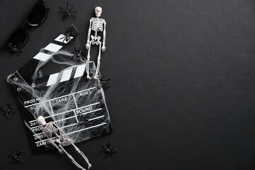 Halloween horror movie concept. Flat lay composition with clapper board in spider webs, skeletons, spider on black background. Top view.