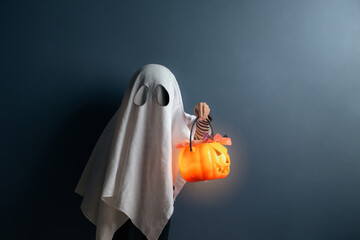 A boy in ghost costume hold a pumpkin head basket with candy at the halloween night.