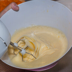 Close-up of the process of beating some eggs with sugar in a white bowl with a stainless steel mixer or beater blades of an electric mixer in the preparation of a cake. Homemade food preparation