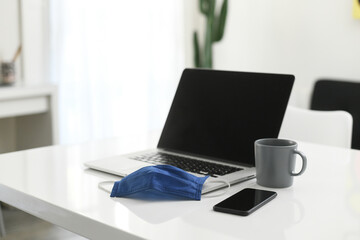 Home workstation during covid-19 lockdown. Homeworking due to virus pandemic emergency. Protective mask on laptop quarantine isolation. Smart working, prevention, health concept. Interior view, nobody