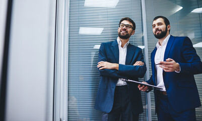 Two Caucasian business partners dressed in formal wear discussing financial strategy during briefing meeting in modern office, successful male entrepreneurs teamworking on collaborative solution