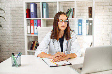 Female doctor with clipboard using laptop at office in the hospital