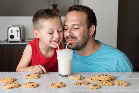Happy father and son sharing a glass of milk with two straws