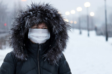 Coronavirus protection at winter, woman in medical mask and fur hood standing on winter street...