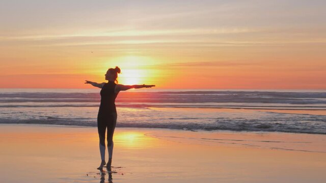 Silhouette of woman with arms raised up having fun on the beach on golden sand