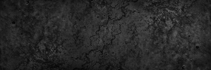 Black grunge stone background. Dark concrete cement texture background. Rough dirty concrete wall surface with cracks. Macro. Black wide grunge banner.