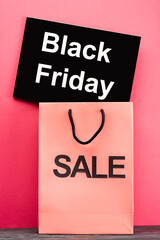 placard with black friday lettering near shopping bag on pink