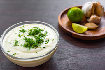 homemade vegetarian mayonnaise garnished with dill, in the background a wooden plate with lime and garlic