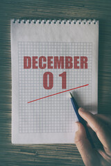december 1st. Day 1 of month,  Close up of human hand with pen on notepad with red underlined date....