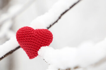 Valentine heart in winter forest, cold weather. Red knitted heart on snow covered branches, symbol of romantic love, background for Christmas holiday