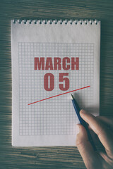 march 5th. Day 5 of month, Close up of human hand with pen on notepad with red underlined date. ...