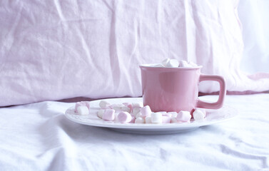 Hot cocoa with marshmallow in a pink ceramic mug on a bed. The concept of holidays and New Year. pink linen background. Flat lay, top view.