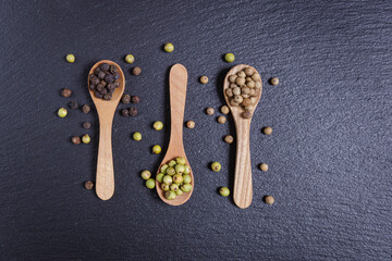 Green pepper, black and whole white peppercorns, pepper mix in wooden spoons, top view