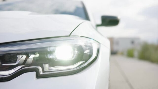 Shining headlight of a white modern car in a suburban area - closeup