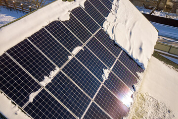 Close up surface of a house roof covered with solar panels in winter with snow on top. Energy...