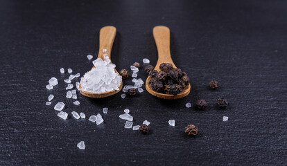 Salt and pepper in wooden spoon, close view