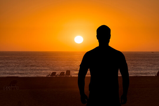 Silhouette of man, back side, in front of sea or ocean during sunset over water, concept picture