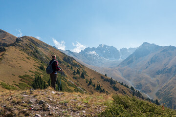 A man with trekking poles and a backpack on the edge of a mountain looking out