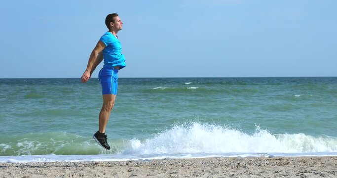 Young man doing jumps at beach working out exercise with ocean background