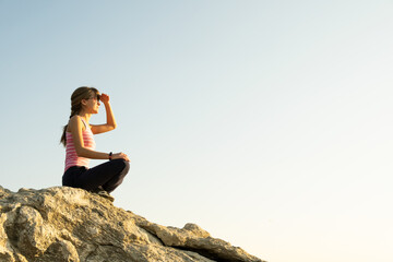 Woman hiker sitting on a steep big rock enjoying warm summer day. Young female climber resting during sports activity in nature. Active recreation in nature concept.