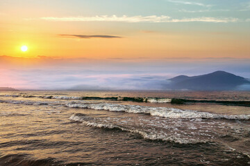 Fototapeta premium Beautiful sunrise in mountains with white fog below and crashing waves of lake water.