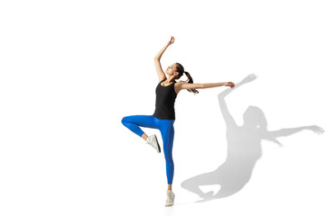 Fototapeta na wymiar High up. Beautiful young female athlete stretching, training on white studio background, portrait with shadows. Sportive fit model in motion and action. Flexibility, healthy lifestyle, style concept.