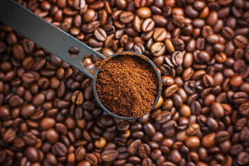 Fototapeta premium On the fragrant coffee beans is a black long measuring spoon, which is filled with ground coffee made from these beans. The view from the top.