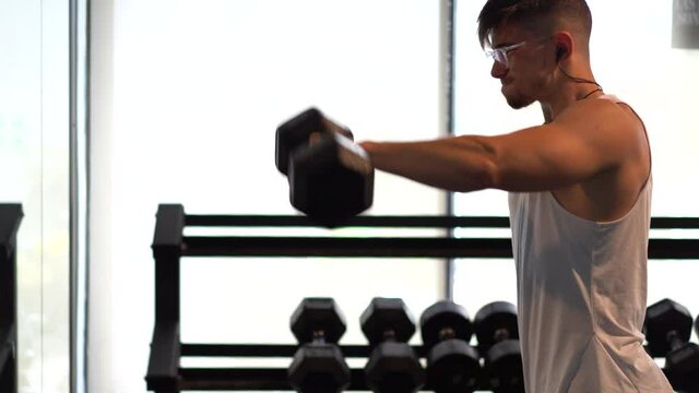 Young hip muscular man lifting dumbbells pumping iron with lateral arm raises in a gym