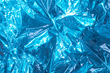 The texture of a thin crumpled sheet of blue foil. Crumpled foil background. Shiny blue foil background. copy space. Selective focus. Blurred background. flatlay