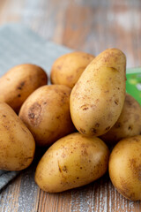 Pile of raw new potatoes on wooden kitchen table with a blue kitchen towel