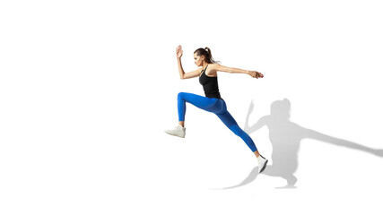 Fototapeta na wymiar High jump. Beautiful young female athlete stretching, training on white studio background, portrait with shadows. Sportive fit model in motion and action. Flexibility, healthy lifestyle, style concept