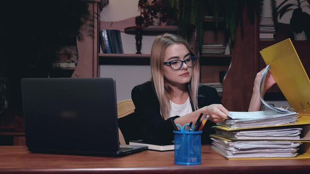 A lot of Paperwork and sad woman. Bored sad worker tired unmotivated and disinterested in dull work with laptop paperwork. Office clerk working, adding folders more work.