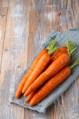 A stack of fresh carrots on country village table with kitchen towel, top view, side view