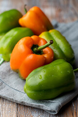 Close up view of assortment of green and orange bell peppers on country rustic tablecloth