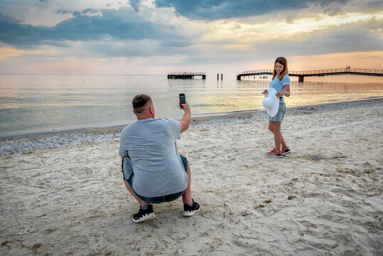 man takes pictures of a woman on a smartphone on the beach