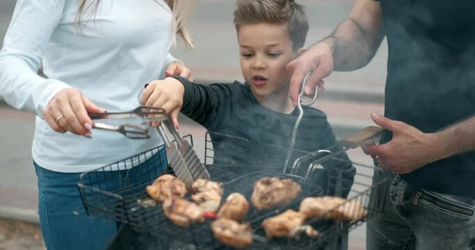 Happy family cook meat on grill. Father and mother with son fry sausages on grill and smiling. Slow motion