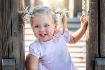 Portrait of a blonde and blue eyed baby girl with pig tails hair having fun on a playground in soft...