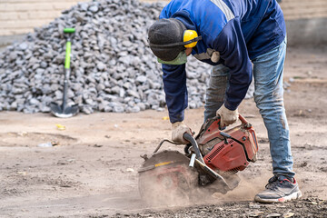Construction worker in safety glasses and noise-canceling headphones at work. Cutting concrete floor for cable laying with a diamond cutting machine.