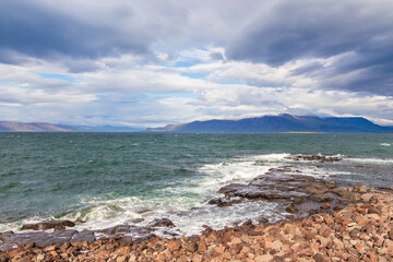 Rocky coast of Faxafloi Bay, mountain in the background, Reykjavik, Iceland.