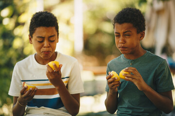 Two brothers african ethnicity sitting outdoors and tasting lemon.