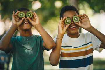 Two african cheerful boys standing outdoors and playing with kiwi fruit.