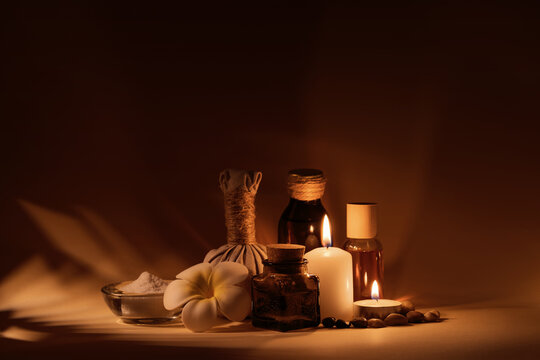 Beautiful spa composition with candles, frangipani flower, oil flasks, bowl with salt and herbal ball.