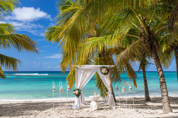Fototapeta na wymiar Wedding bamboo gazebo, decorated with tropical flowers and coloured fabrics on the paradise beach with palm trees, white sand and blue water of Caribbean Sea, Punta Cana, Dominican Republic 