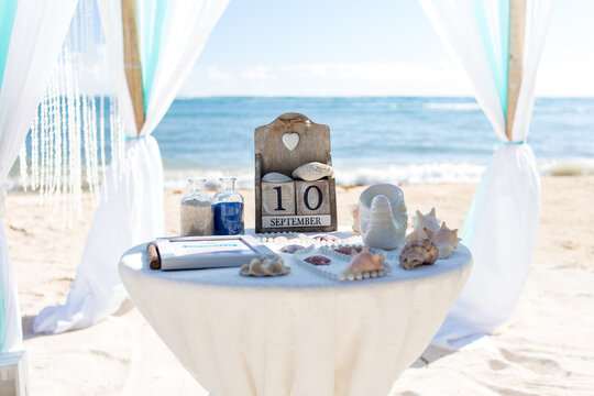 Close up view of table for the beach wedding ceremony with decoration of shells, jars with color sand, wooden calendar inside bamboo gazebo, Punta Cana, Dominican Republic