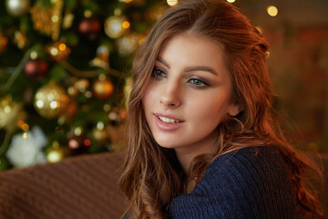 Close up portrait of a young beautiful smiling woman posing in an interior with festive Christmas lights on the background.