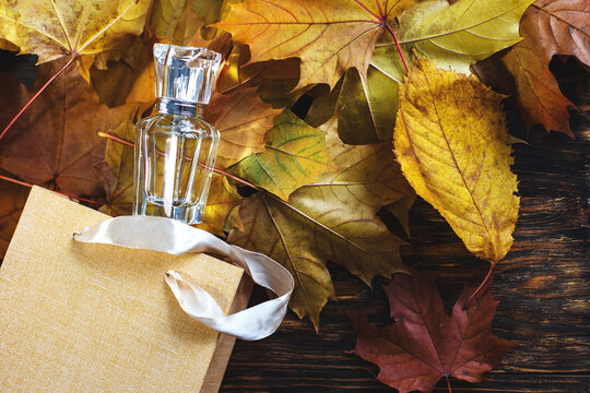 A Glass Bottle Of Female Perfume With Gift Bag Laid On Autumn Yellow Leaves On A Wooden Background. Natural Perfumery.